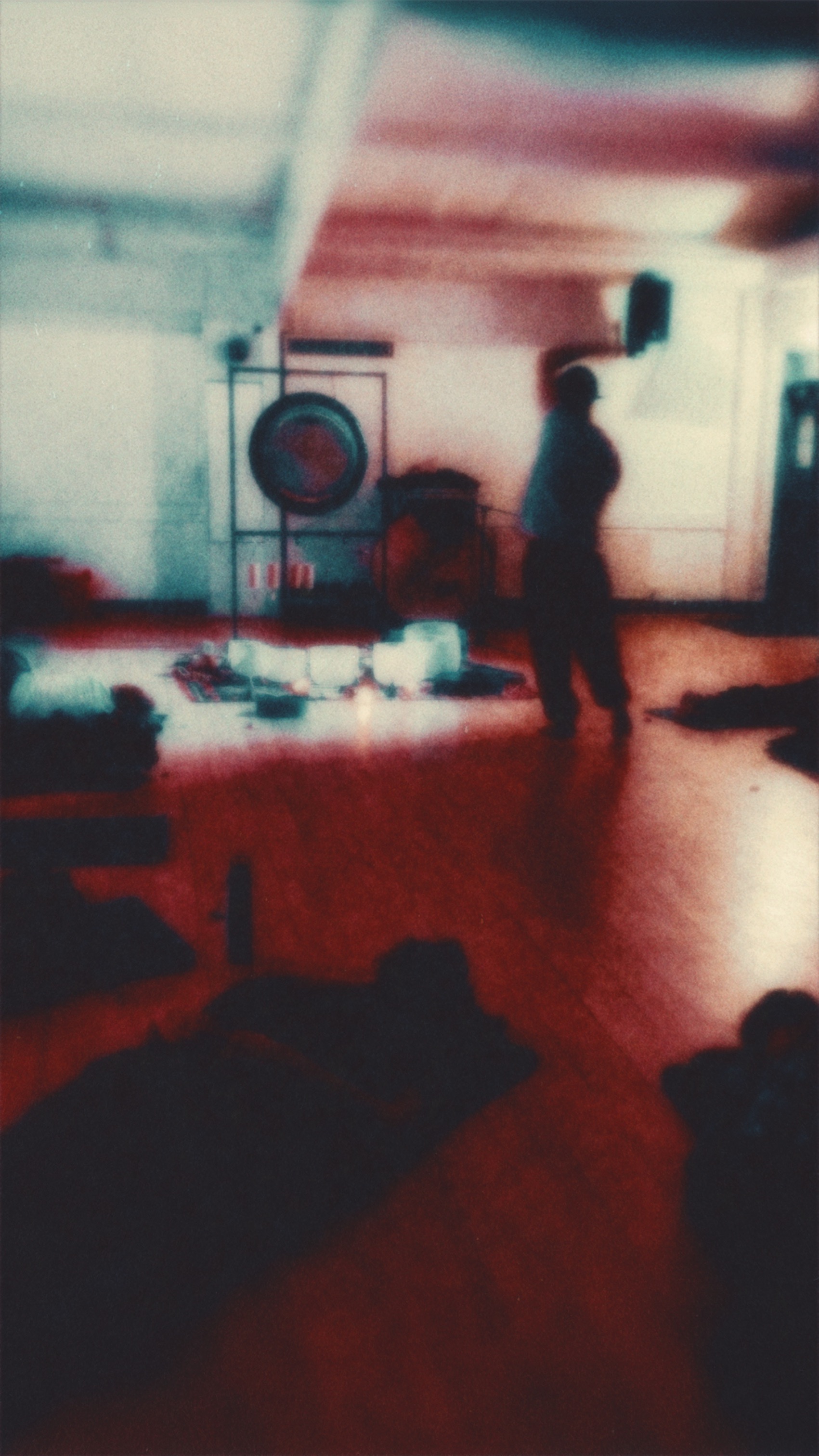 Moody long exposure of a soundbath setup; blurred figure near a gong with teal and red trails.