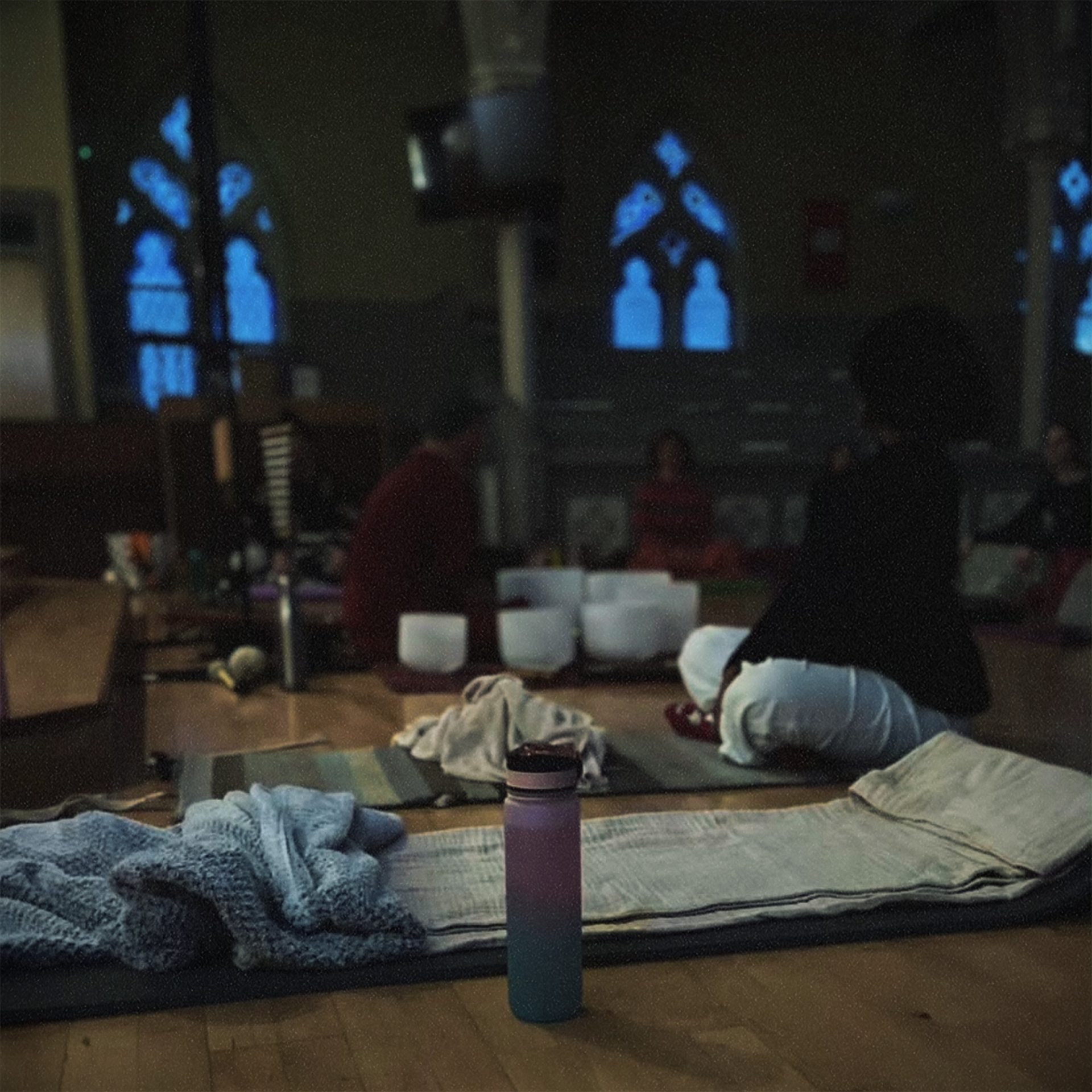 Participant’s view from a mat with blanket and bottle; bowls and people softly out of focus ahead.
