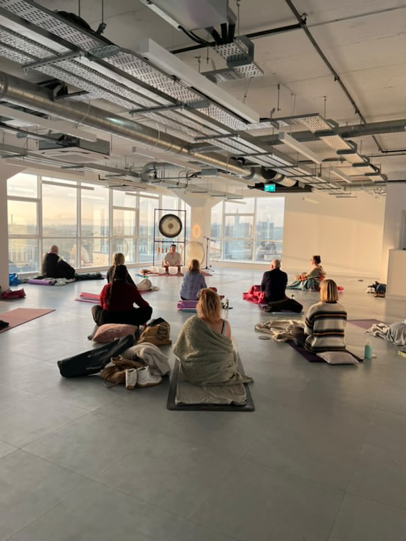 Group seated for a soundbath in a high-floor space with panoramic city views and industrial ceiling.