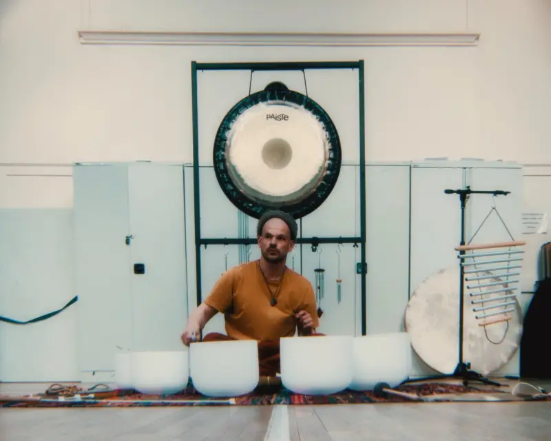Iain playing crystal bowls beneath a large Paiste gong in a bright white hall.